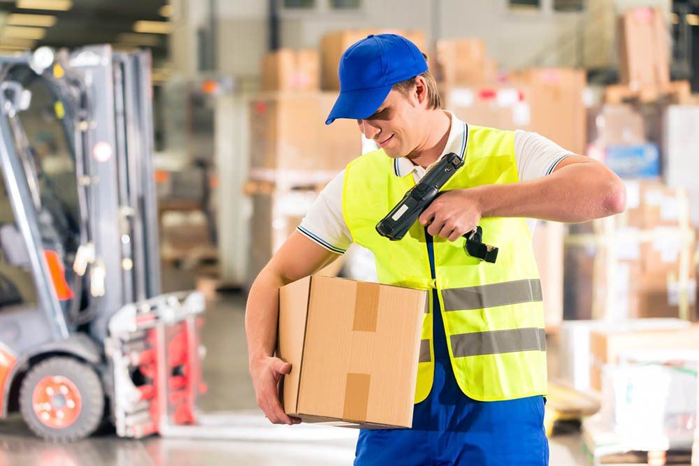 A man is holding a box and using a scanner in a warehouse.