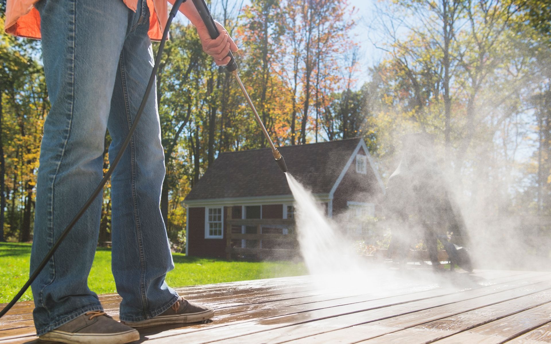 A man is using a high pressure washer to clean a wooden deck.