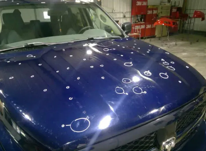 Blue car hood covered in small dents, each circled with white paint, in a repair shop. | Jacobson Body Shop
