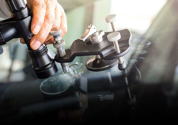 Person repairing a windshield crack with a specialized tool, close-up view. | Jacobson Body Shop