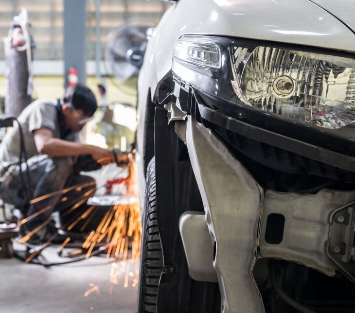 Car with damaged front bumper; mechanic welding in a repair shop. | Jacobson Body Shop