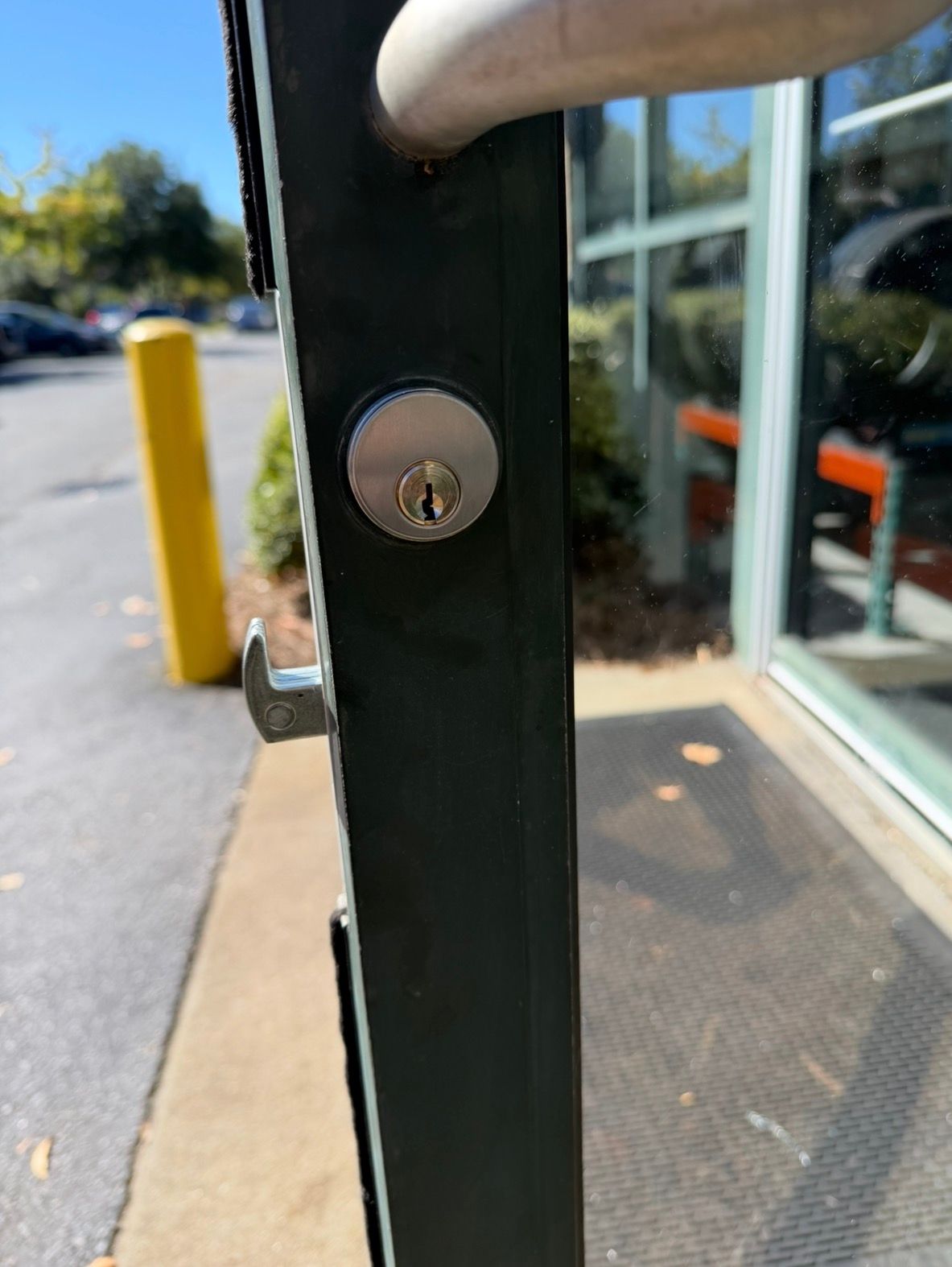Man in blue shirt opens a glass door, holding a laptop case, in an office setting.