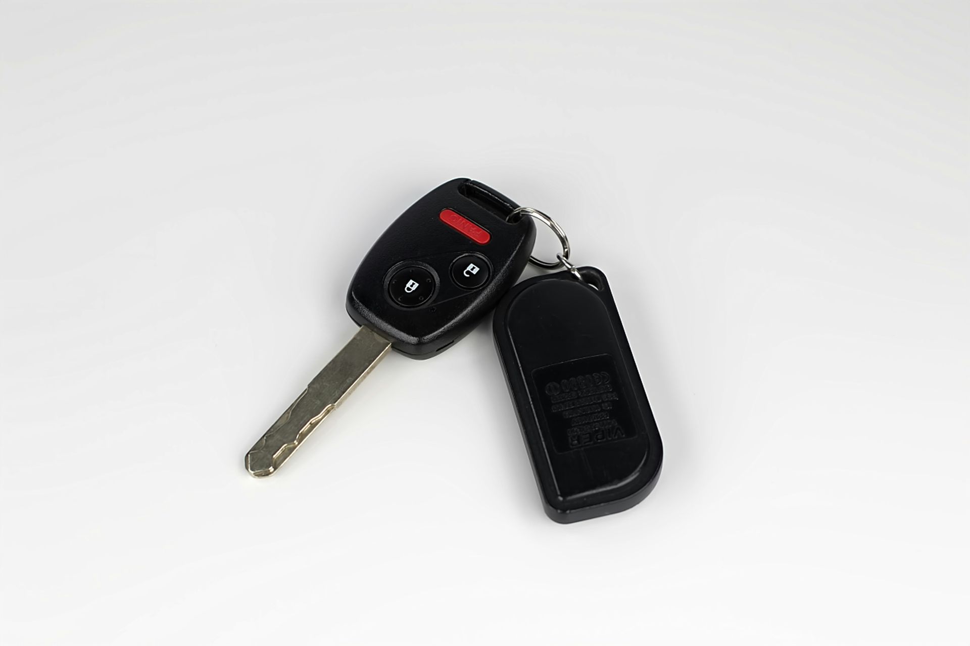 A car key and remote control are on a white surface.