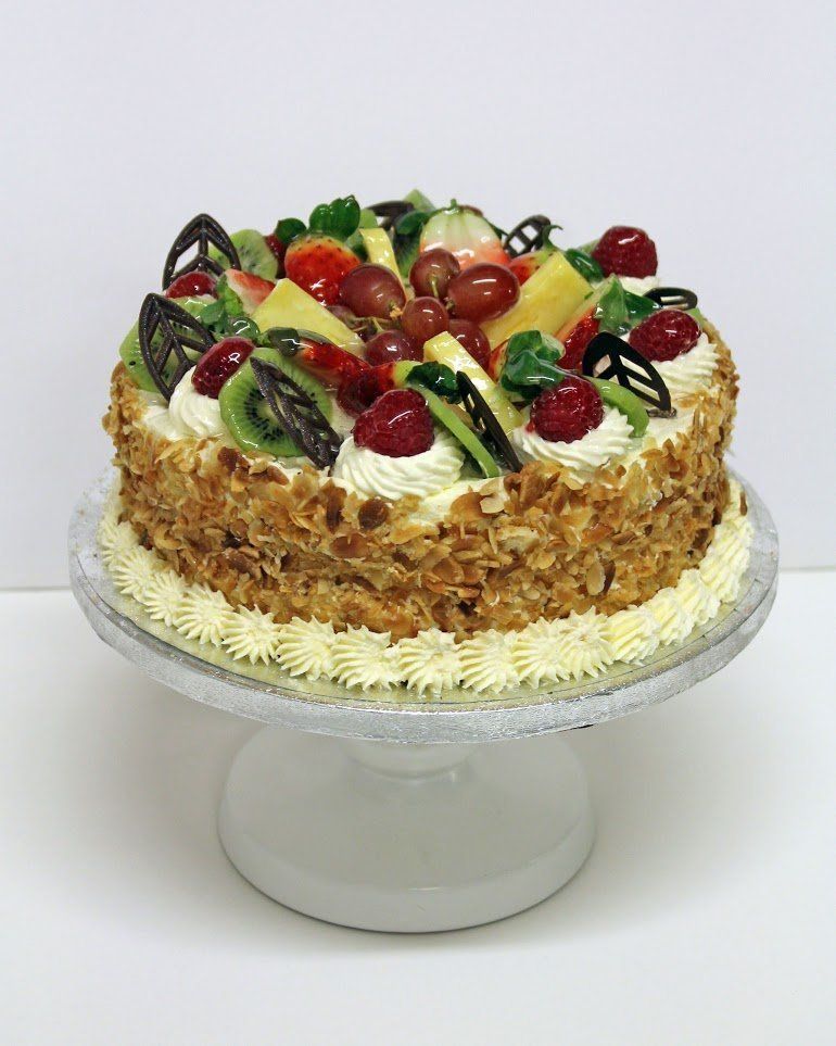 A fruit-topped cake with almond-covered sides, decorated with whipped cream and chocolate
