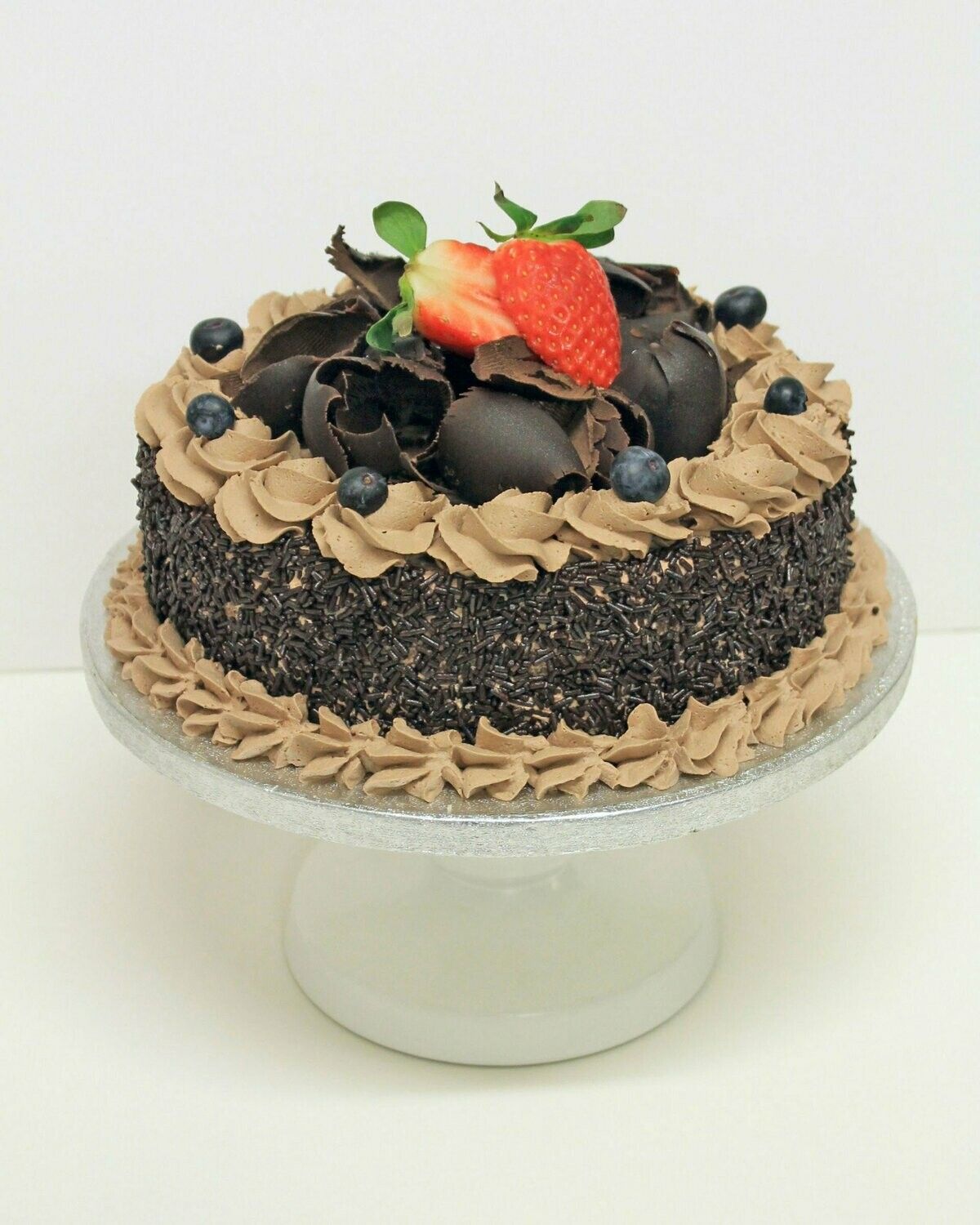 A round chocolate cake topped with chocolate curls, blueberries, and fresh strawberries