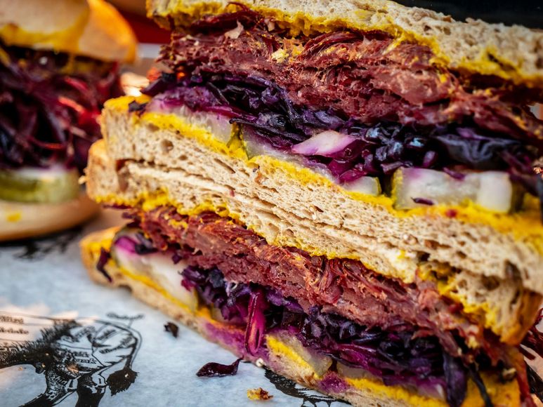 A close up of a sandwich with meat and vegetables on a table.