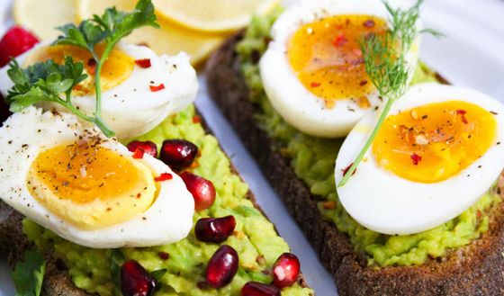 Two slices of avocado toast with hard boiled eggs and pomegranate seeds.