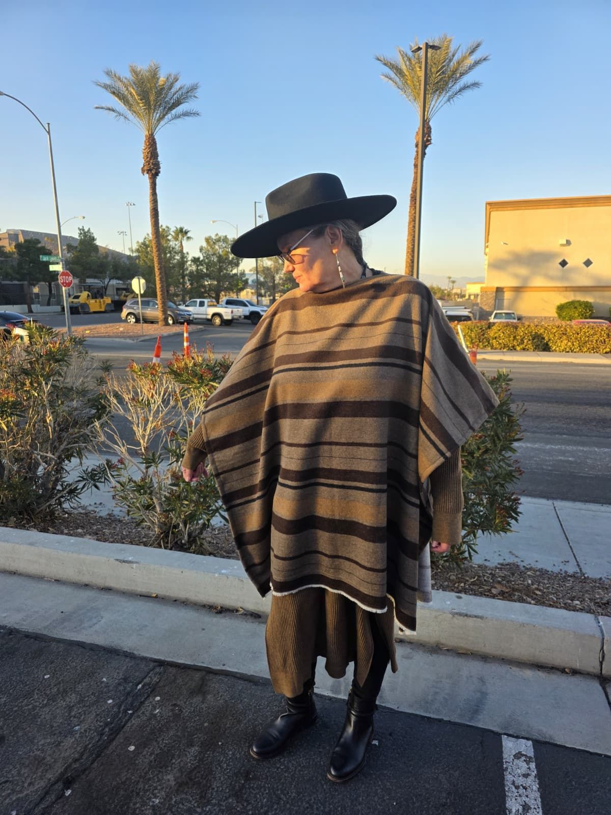 Person wearing a black hat and poncho stands near a road with palm trees.