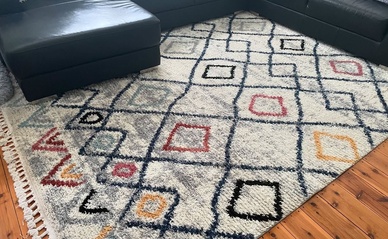 A shaggy, off-white area rug with a black diamond grid pattern and colorful square accents on a wooden floor  — Cobra's Carpet Cleaning in Junee, NSW