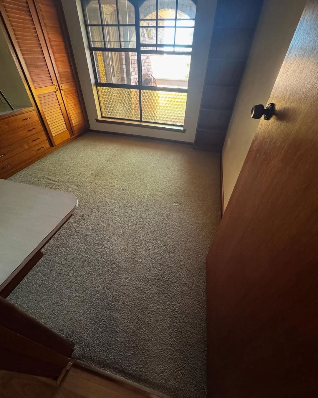 An Empty Carpeted Bedroom With Wooden Cabinets, a Large Grid Window — Cobra's Carpet Cleaning in Junee, NSW