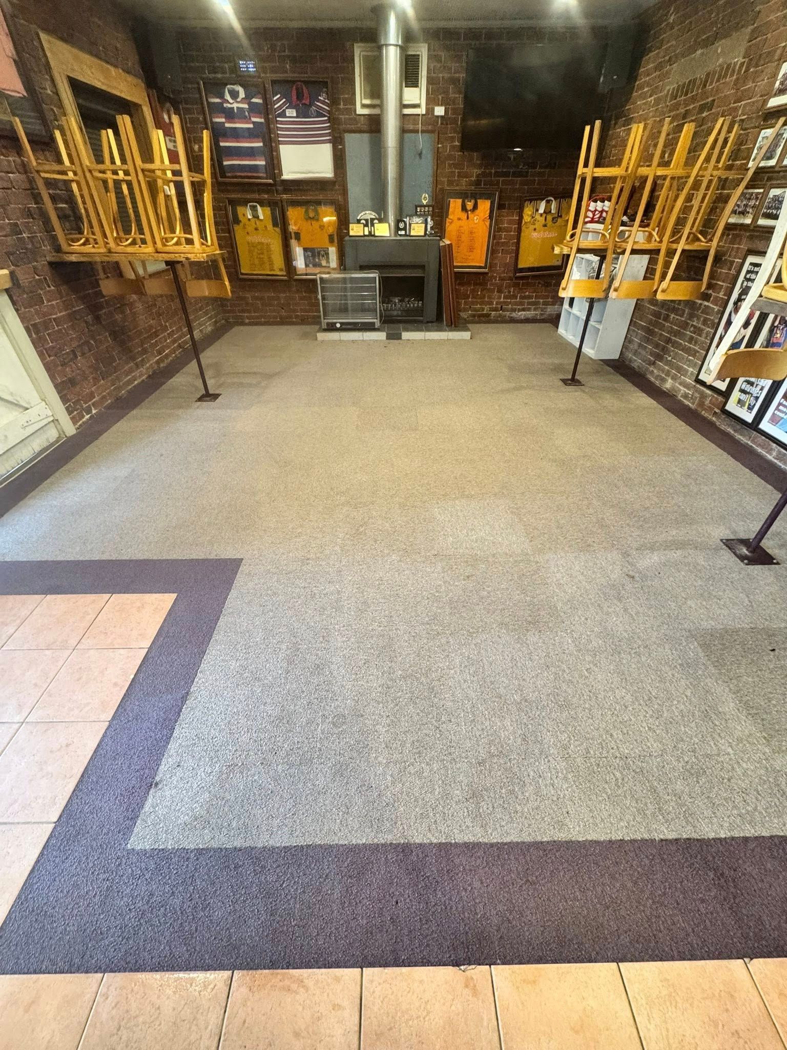 A restaurant dining area with tables pushed aside, grey carpet, brick walls, and jerseys displayed on the back wall  — Cobra's Carpet Cleaning in Junee, NSW