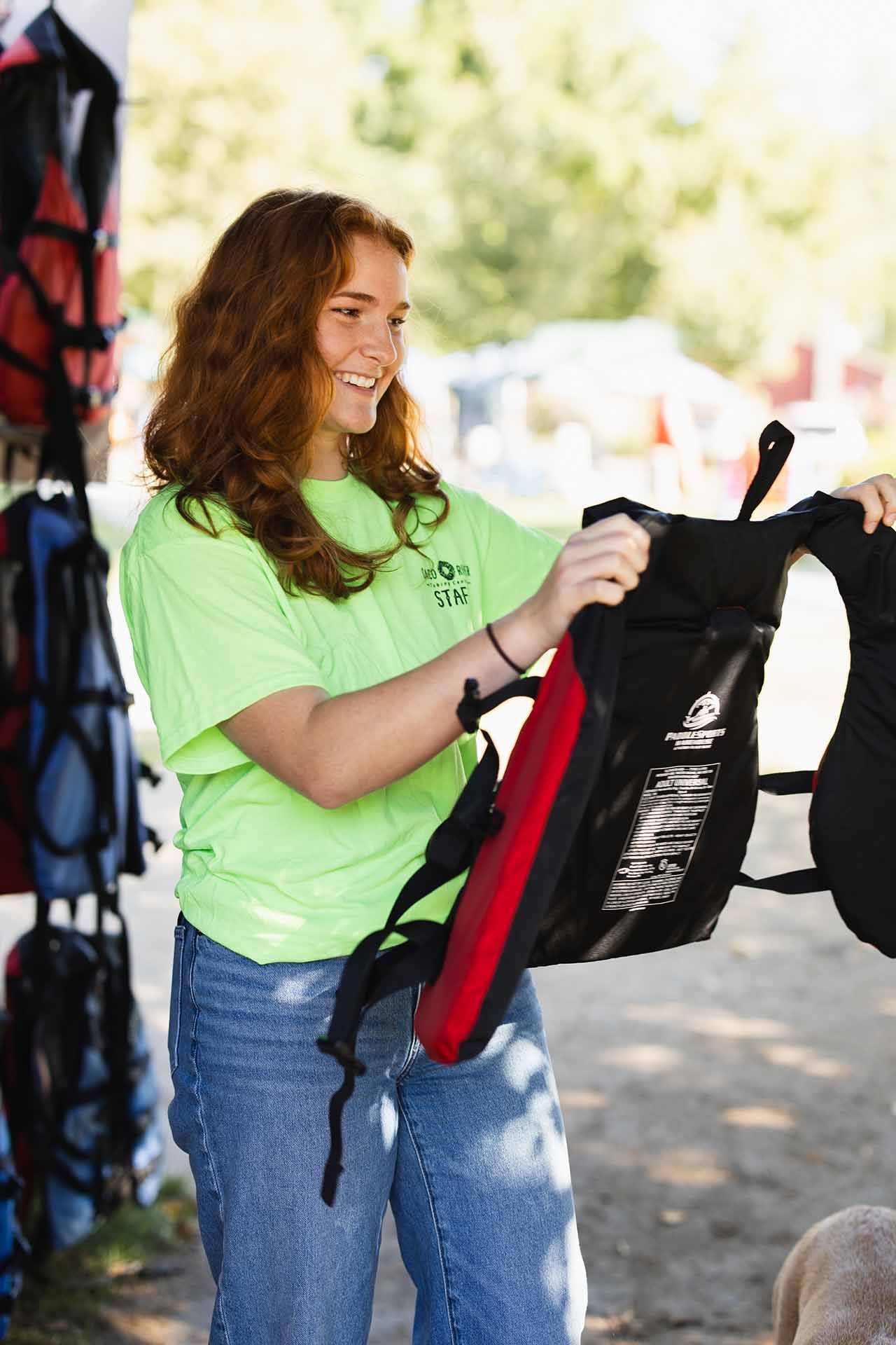 Woman in A Green Shirt Holding a Black and Red Life Vest