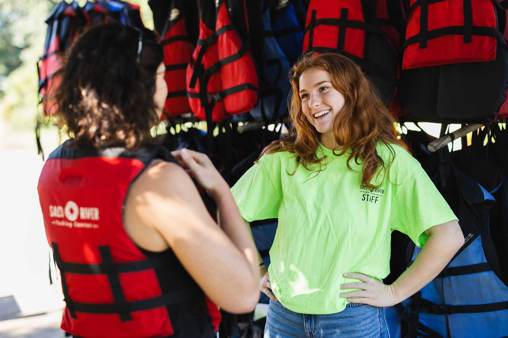 A woman in a green shirt is talking to a woman in a life jacket.