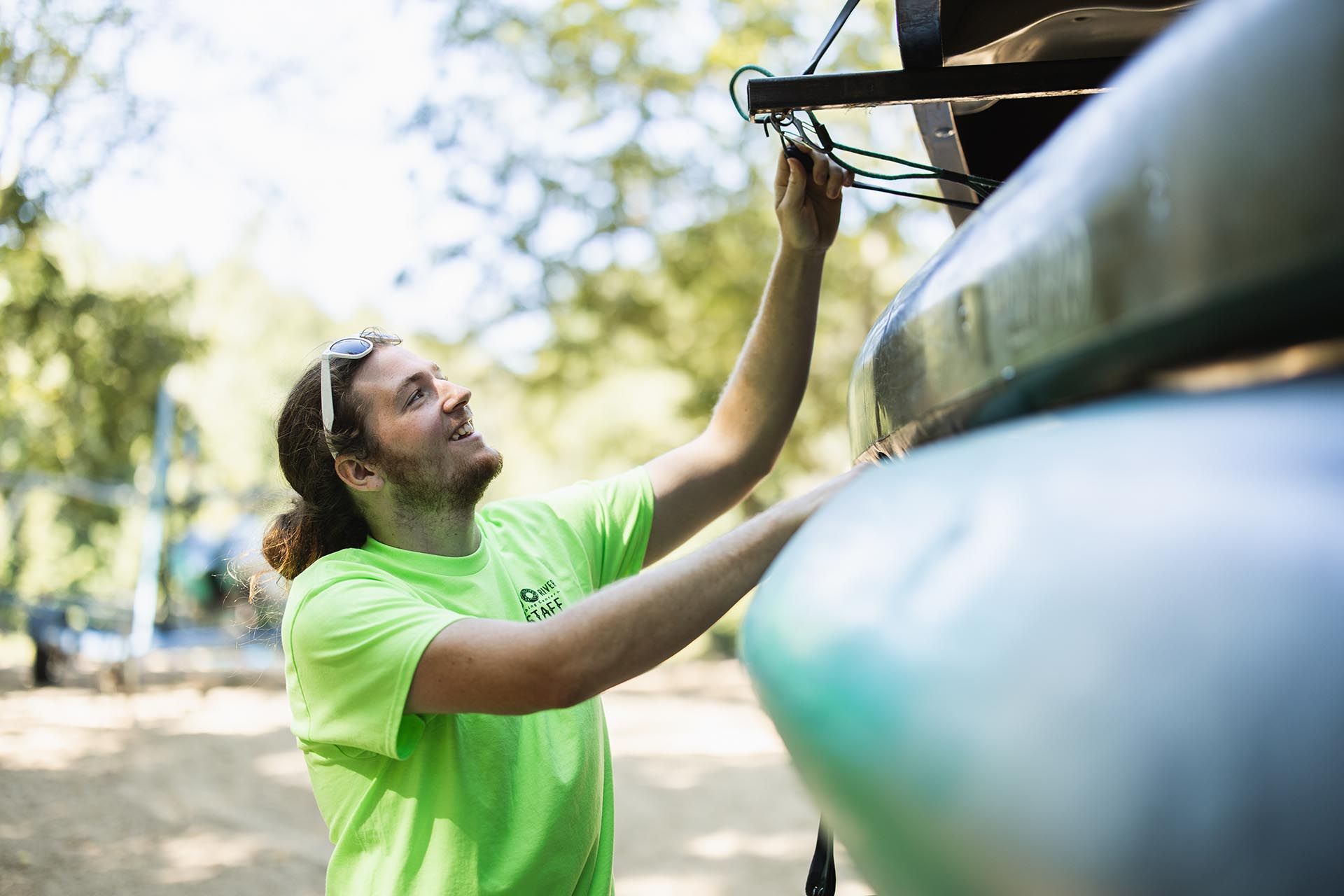 A Man in A Green Shirt Is Hanging a Kayak on A Rack