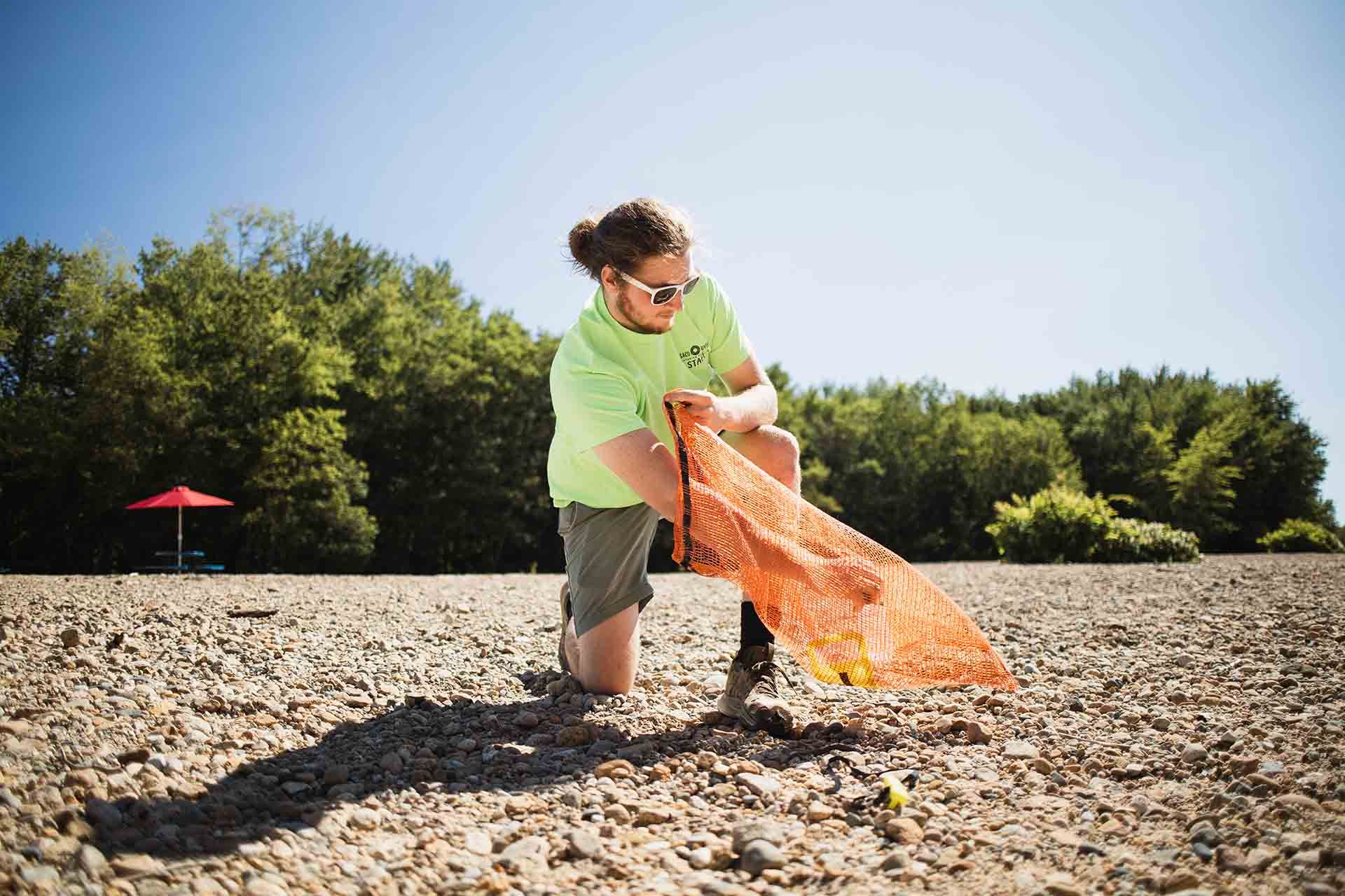 Man Kneeling Down on A Rocky River Cleaning up Trash