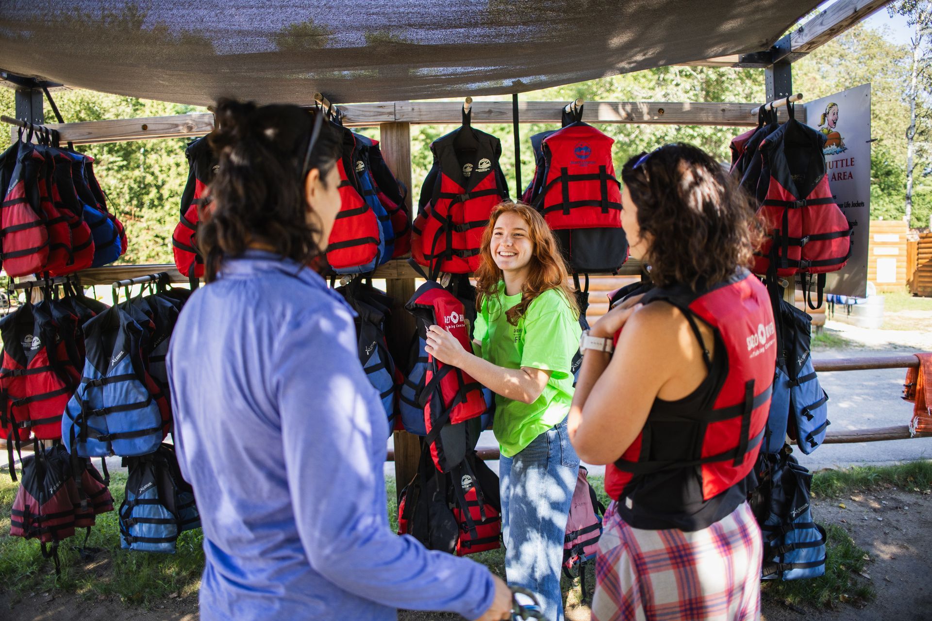 A person helps to select life jackets by the river