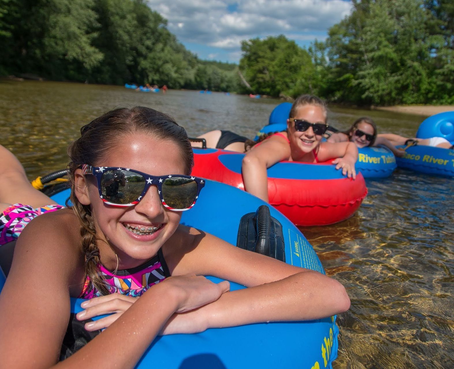 Two smiling kids wearing sunglasses floating in a shallow part of a river