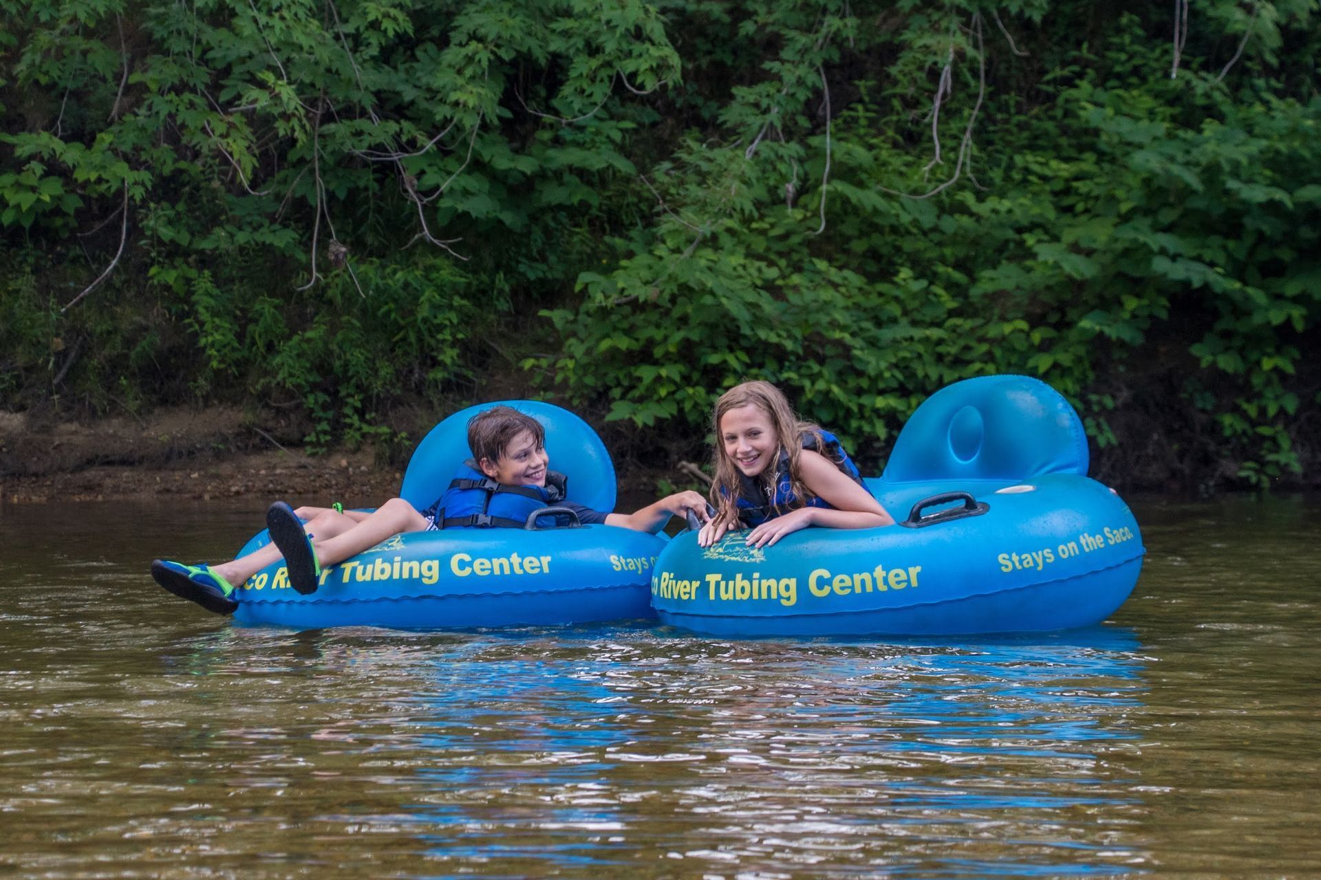 A boy and a girl are floating on a tube in the water.