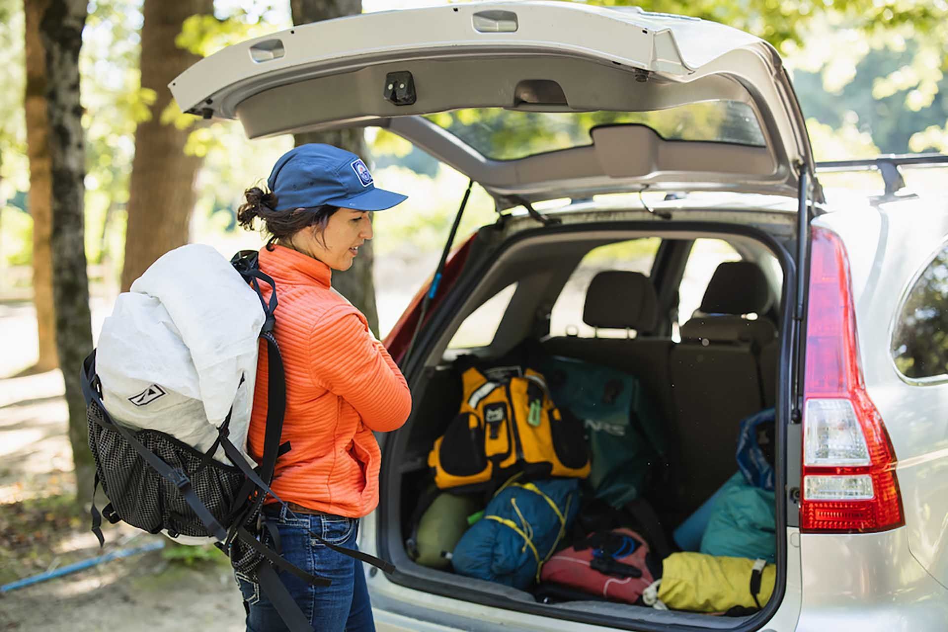 a woman packing the back of a car with camping items 