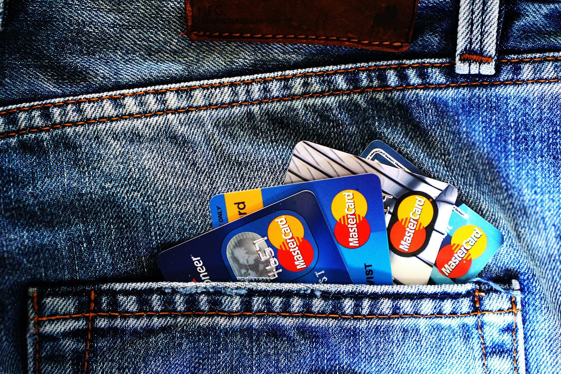 Several credit cards including a mastercard are in the back pocket of a pair of jeans