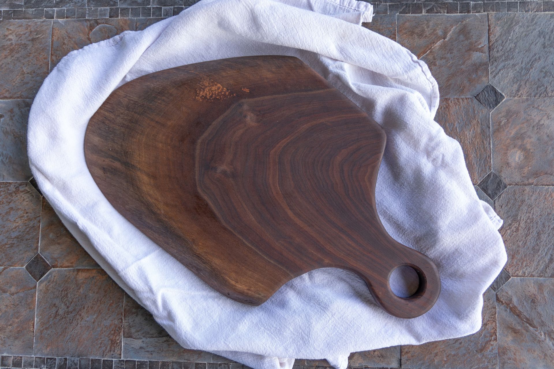 Two walnut cutting boards rest on a white towel, on a tiled surface.