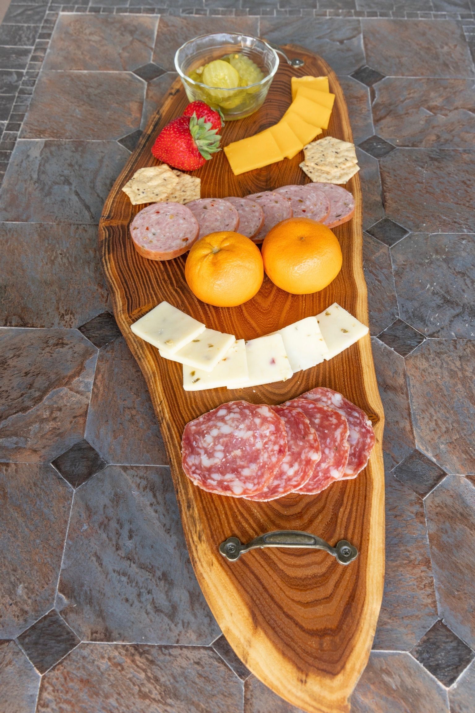 Charcuterie board with salami, cheese, fruit, crackers, and pickles on a wooden surface.