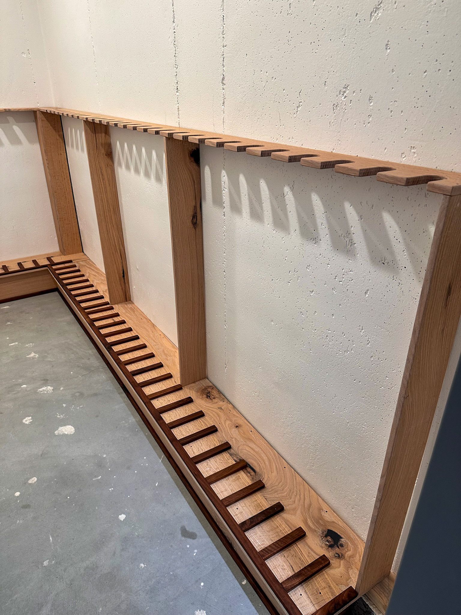 Wooden framing with a ladder-like pattern against a textured white wall, on a gray concrete floor.