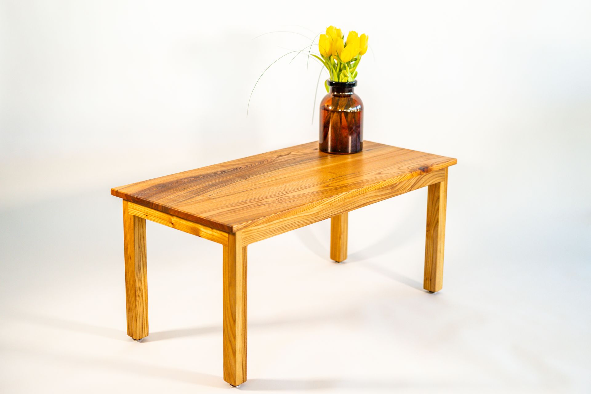 Wooden table with a vase of yellow flowers on a white background.