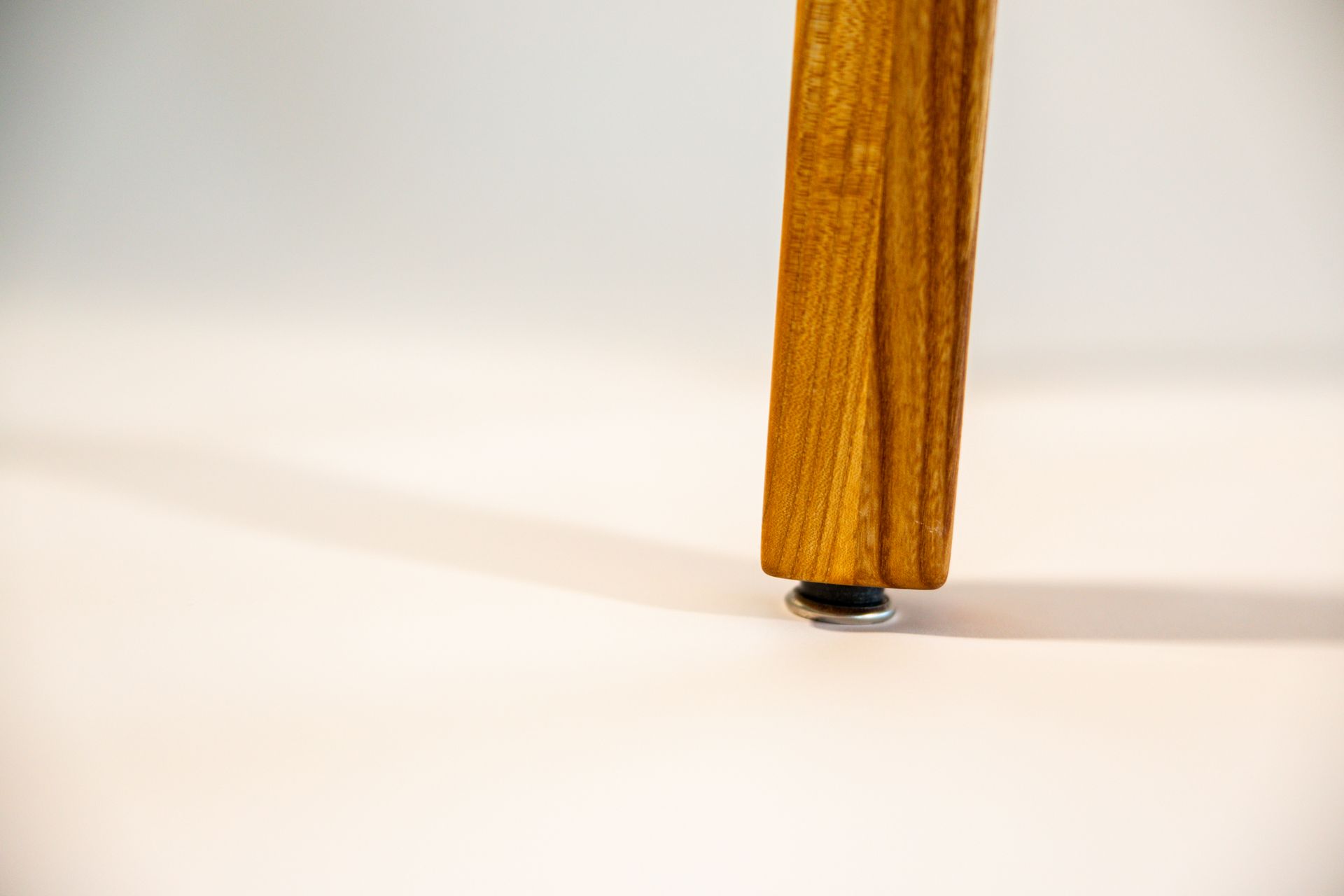 Wooden chair leg with a small, silver foot on a white surface.