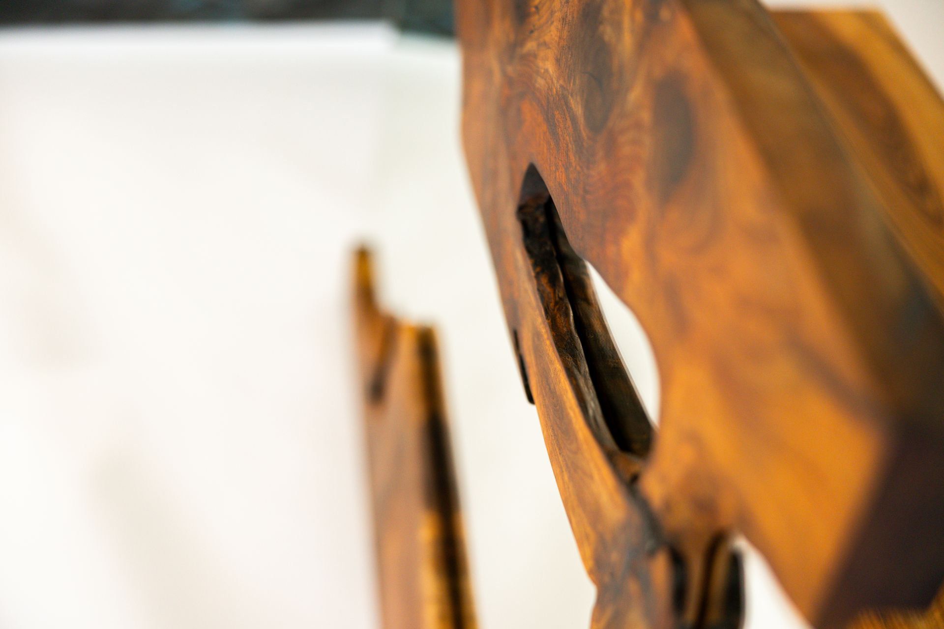 Close-up of carved wooden art piece with a dark, rich finish, mounted against a white wall.