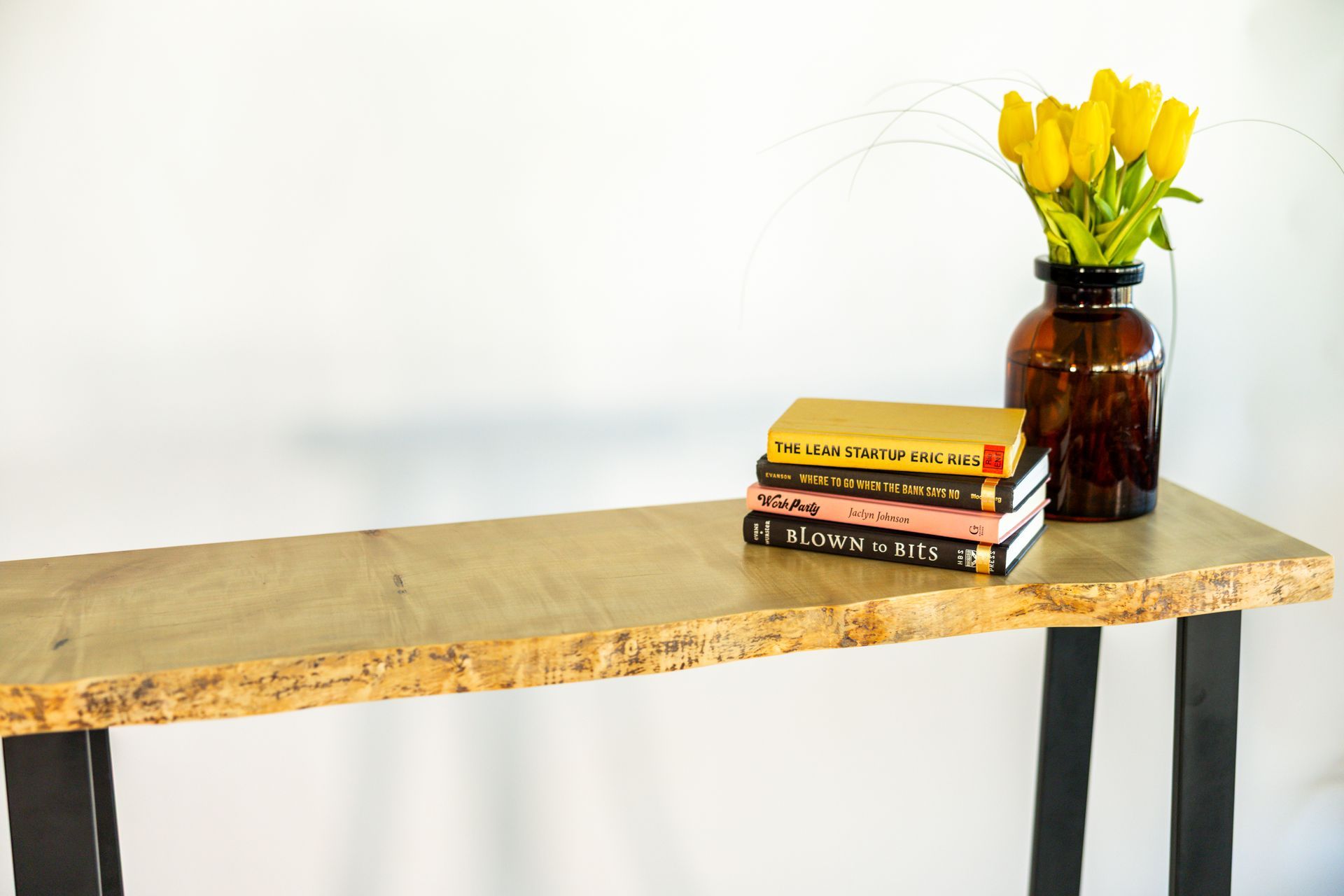 Wooden console table with books and a vase of yellow tulips.
