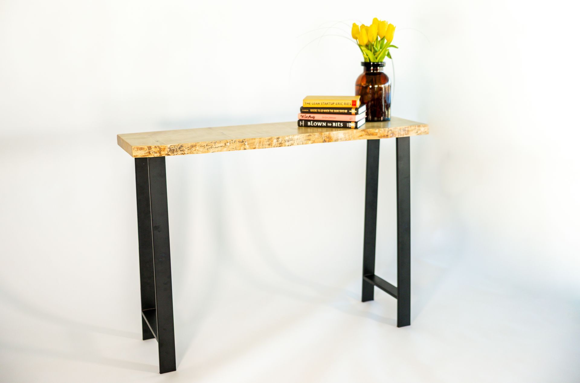 Narrow console table with light speckled top and black metal legs, topped with books and a vase of yellow flowers.