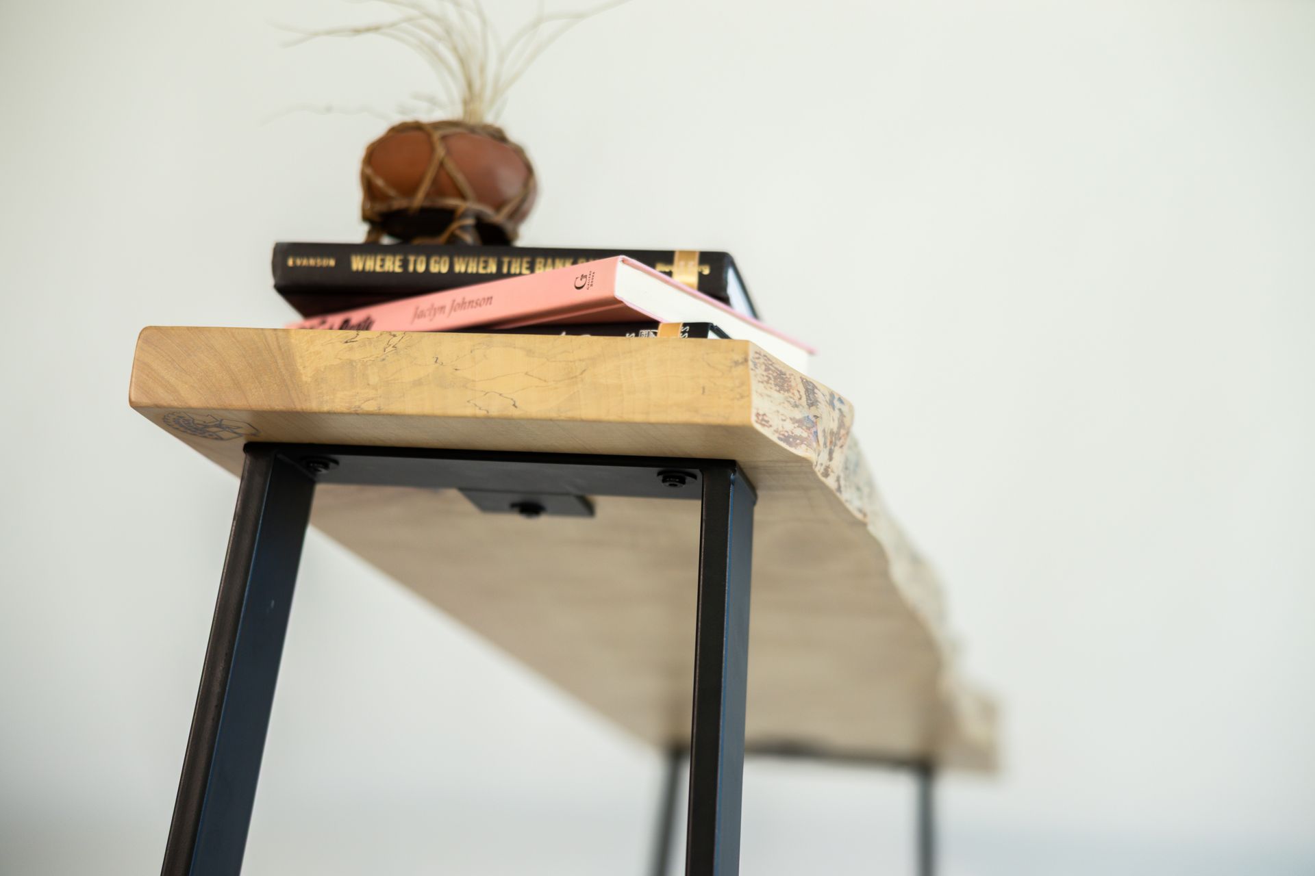 Wooden shelf with black legs, topped with books and a small vase with a plant.