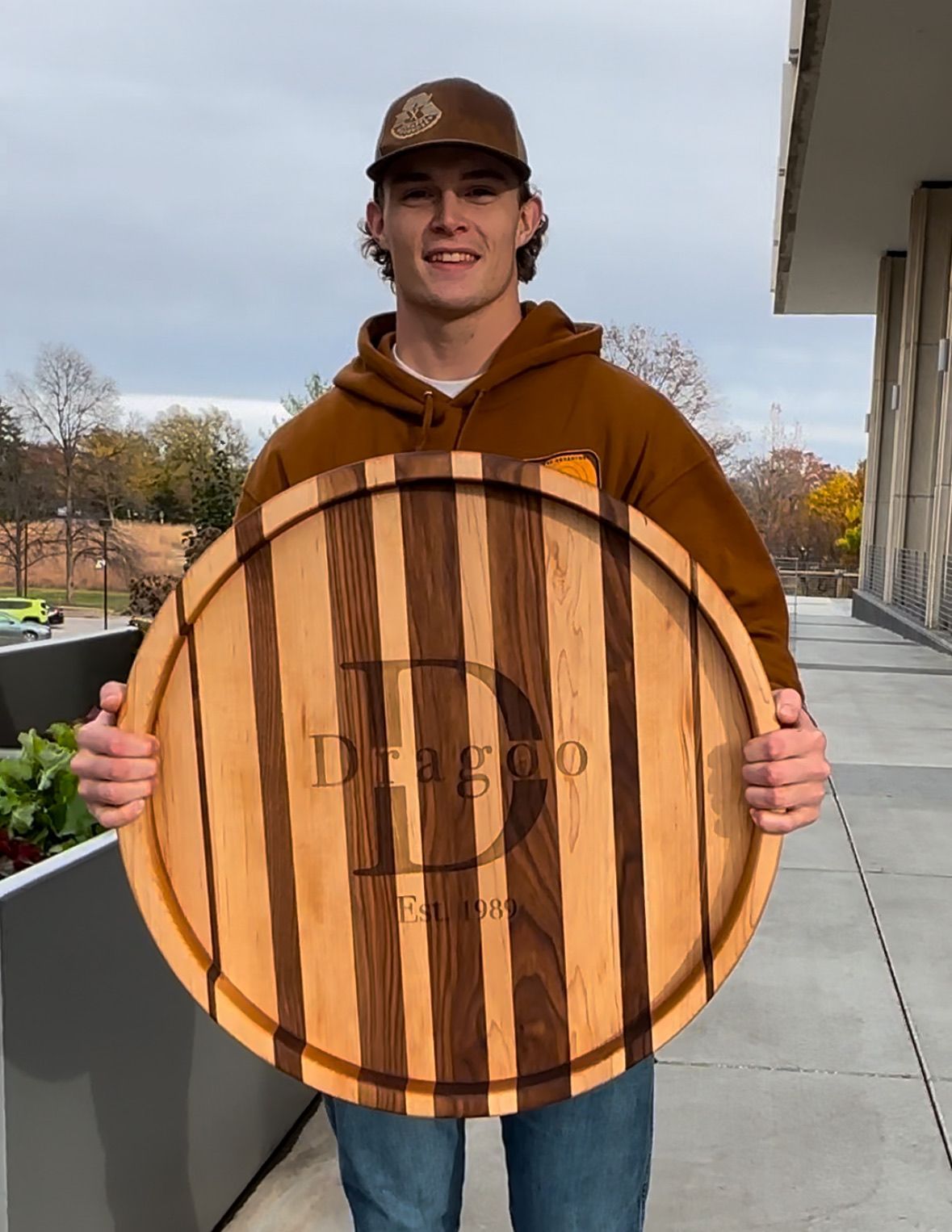 Young man holding a large, striped wooden serving board engraved with 