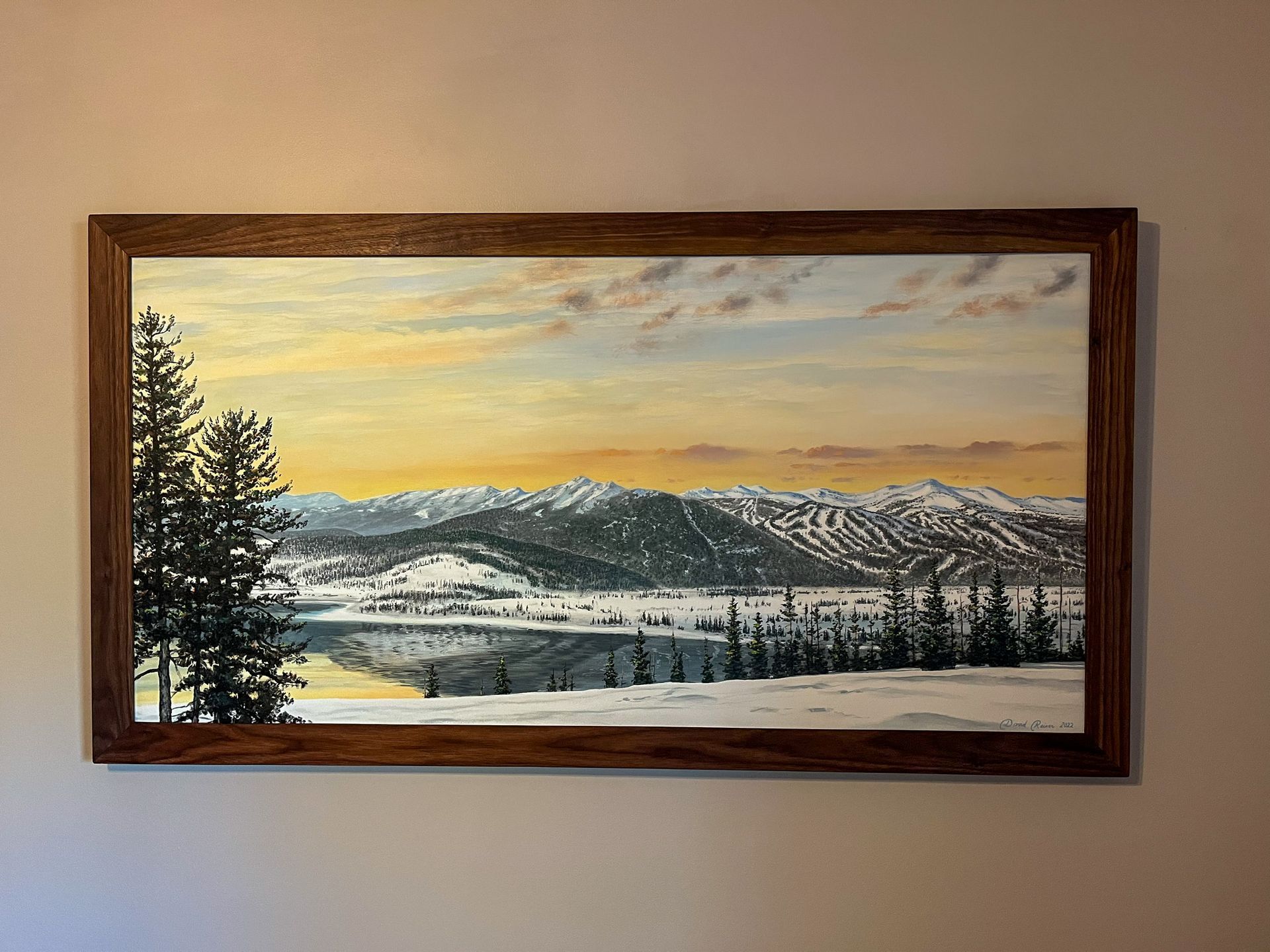 Winter landscape painting, snow-covered mountains, evergreen trees, and lake at sunset. Wooden frame.