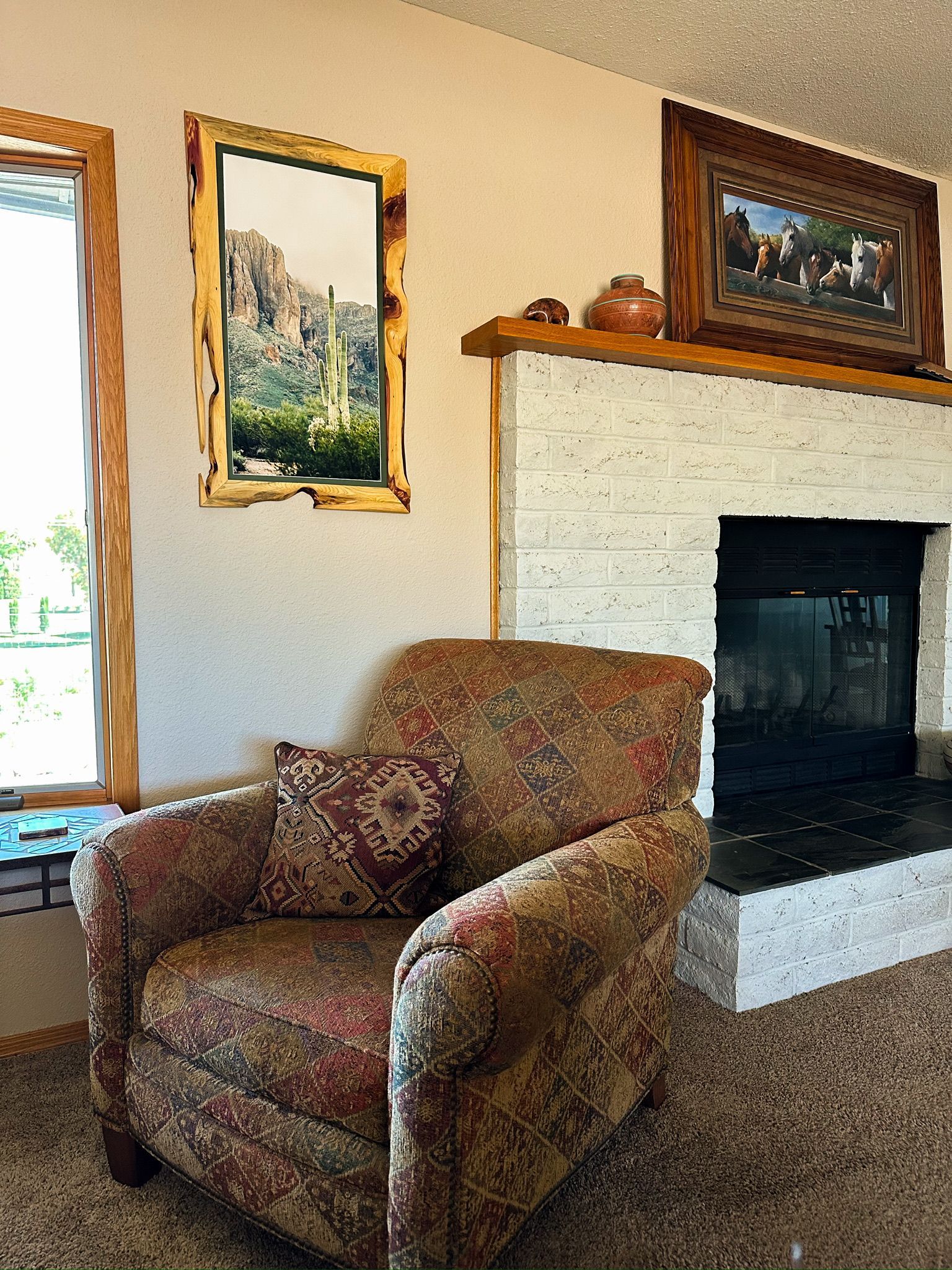 Cozy living room with armchair, fireplace, artwork, and window.