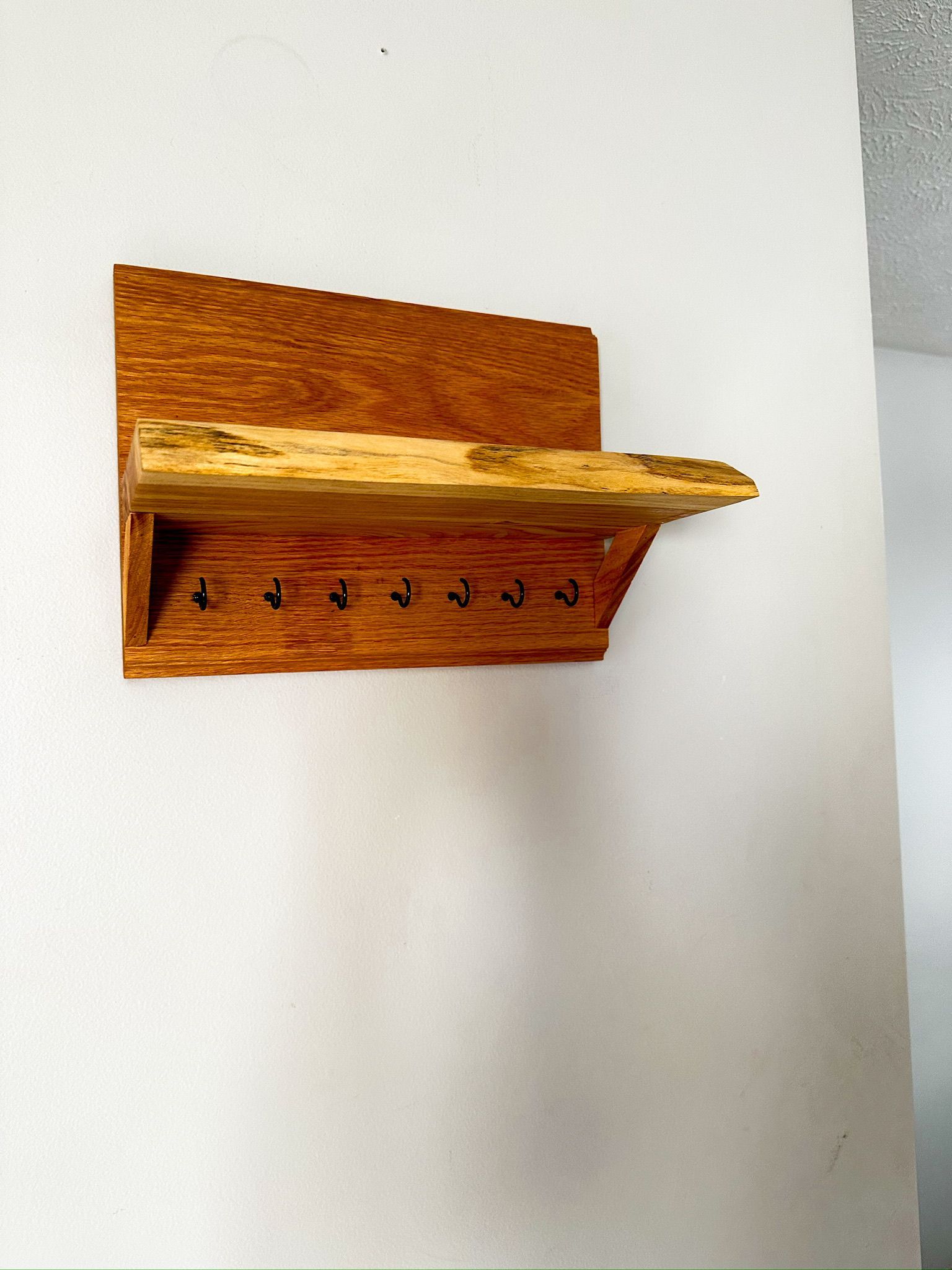 Wooden key holder with shelf mounted on a white wall, featuring hooks and a natural wood finish.