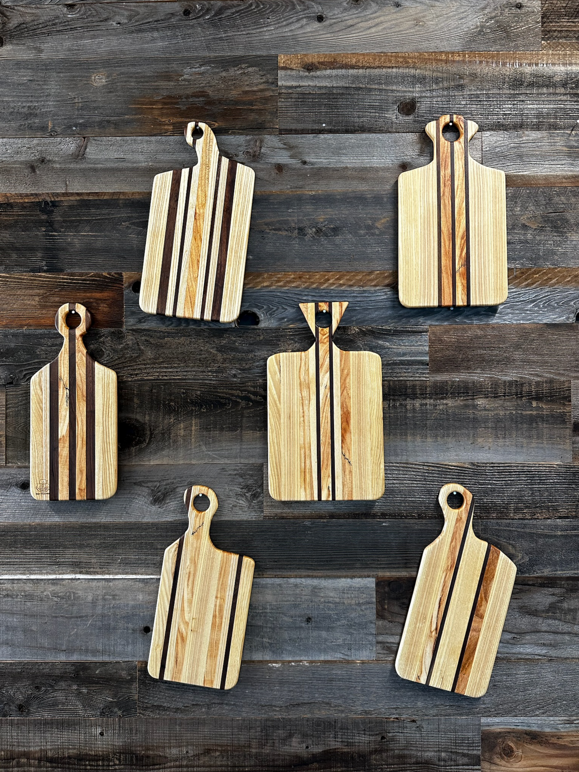 Wooden cutting boards with various striped designs, hanging on a weathered wood wall.