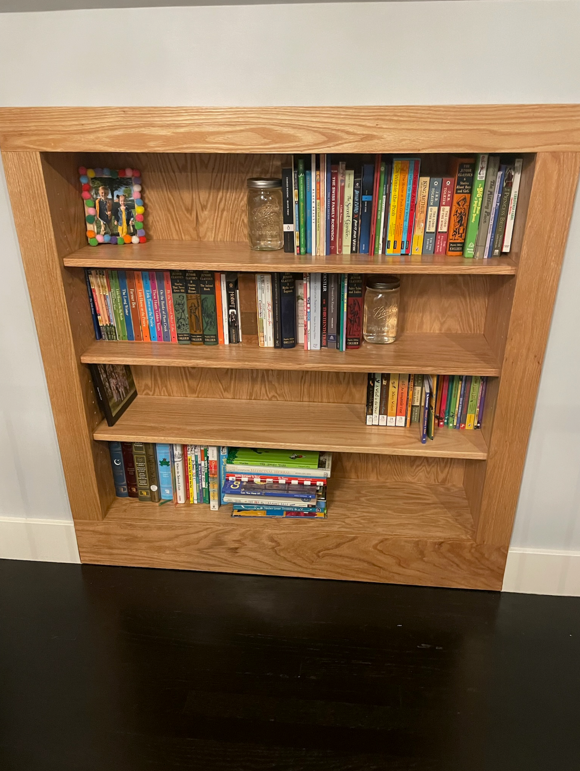 Built-in wooden bookshelf filled with colorful books, mounted in a wall.