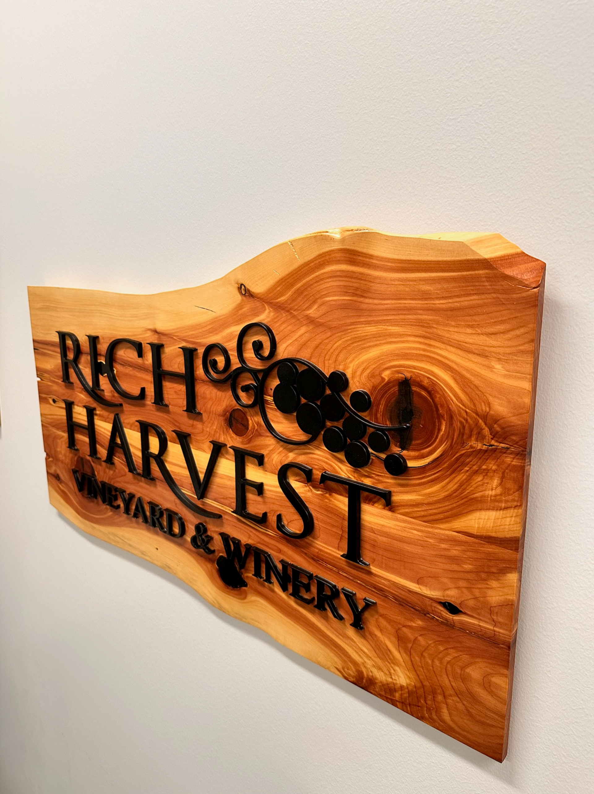 Wooden sign for Rich Harvest Vineyard & Winery, with black lettering and grape design, mounted on a wall.