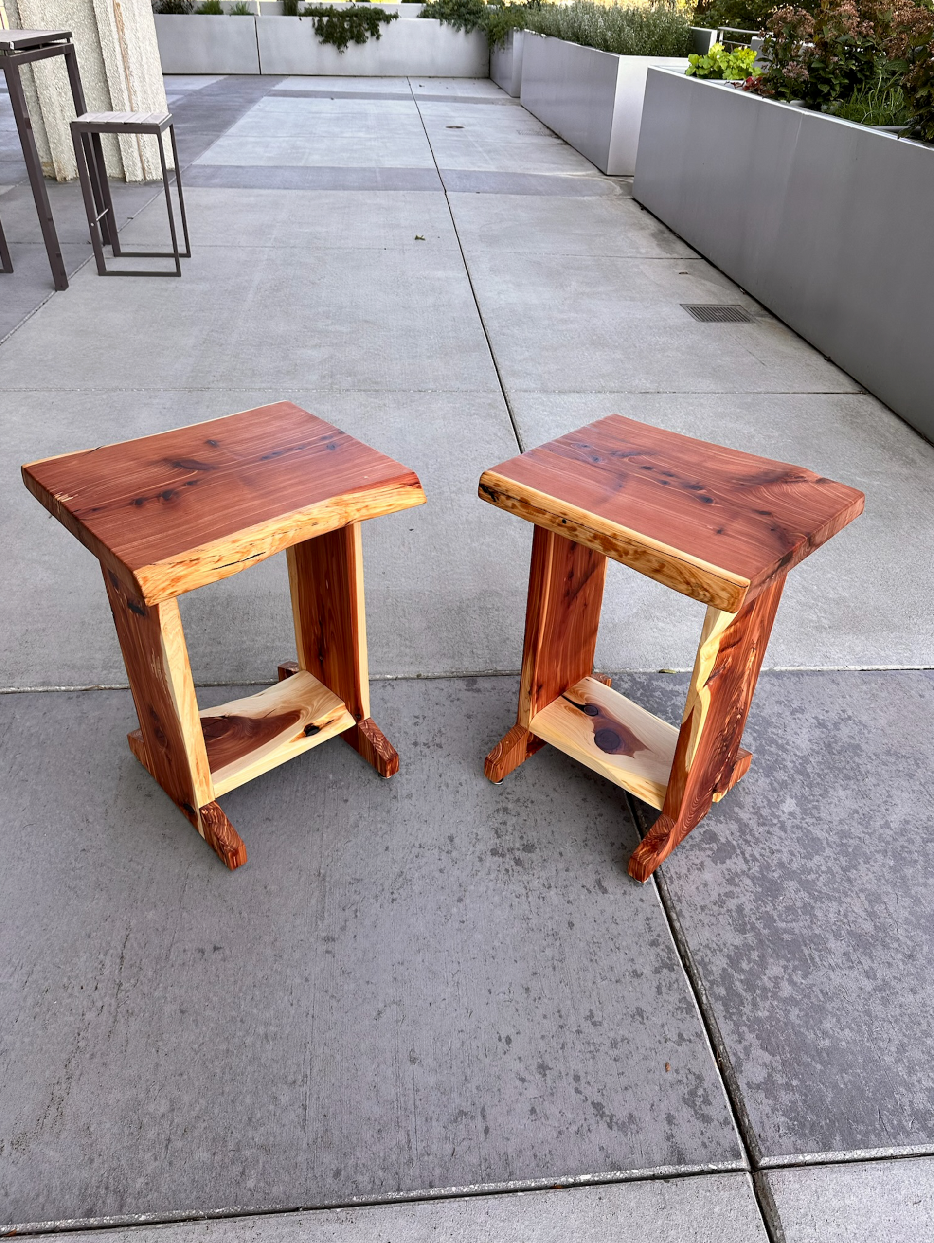Two handcrafted, wooden side tables with live edges, on a concrete patio.