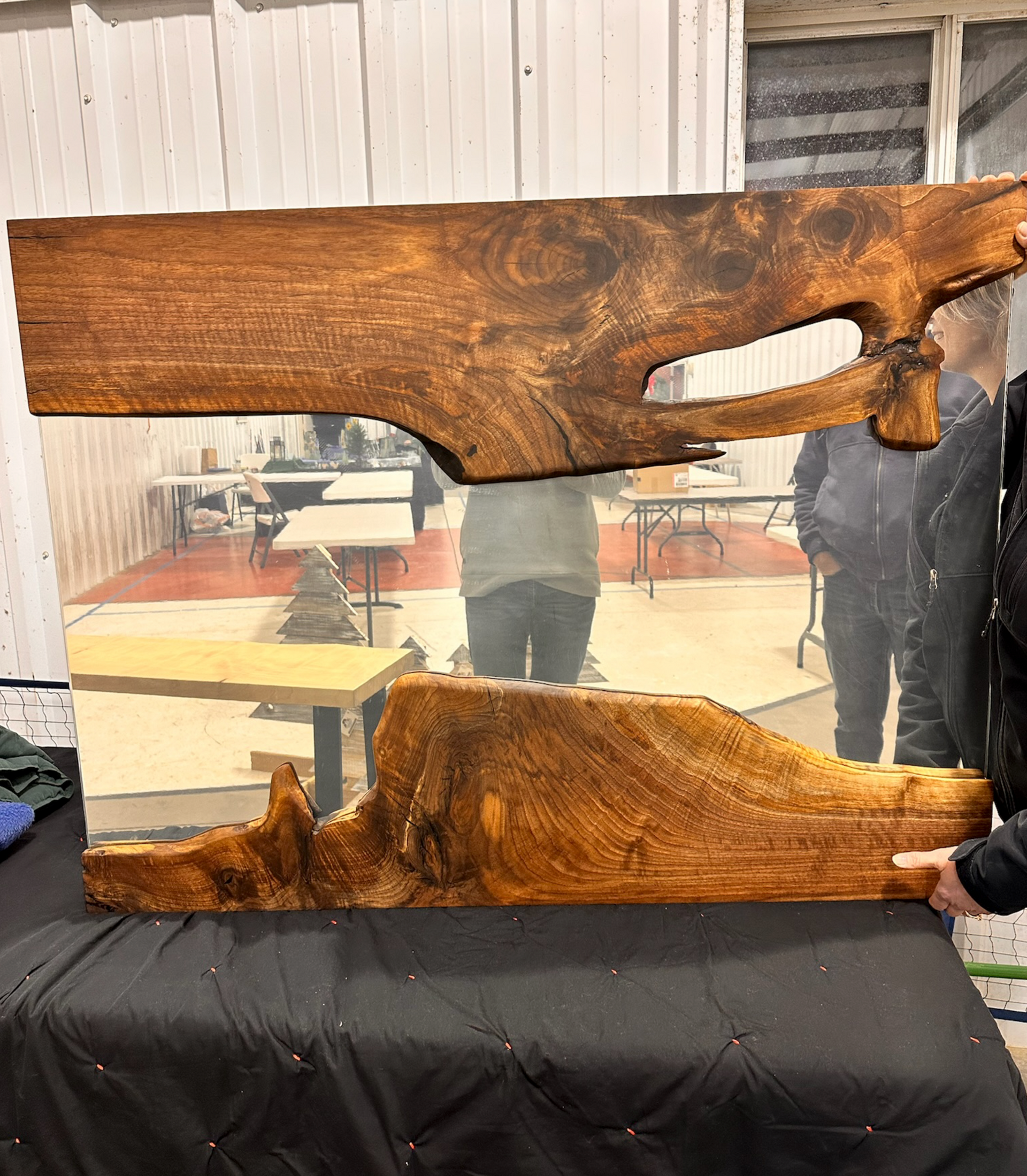 Large wooden-framed mirror with organic edges, reflecting a person and a room, held by a person. Brown wood, clear glass.