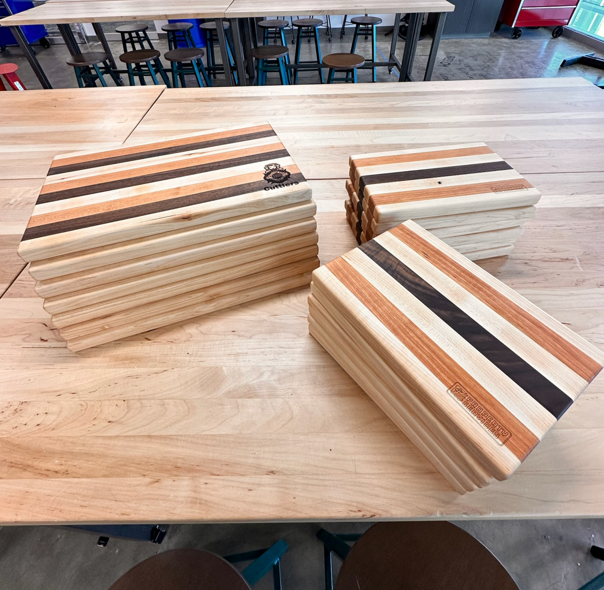 Stacks of handmade striped wooden cutting boards on a light-colored wood surface.