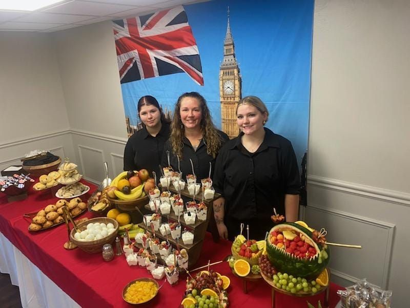 Three women are standing in front of a table with fruit on it.