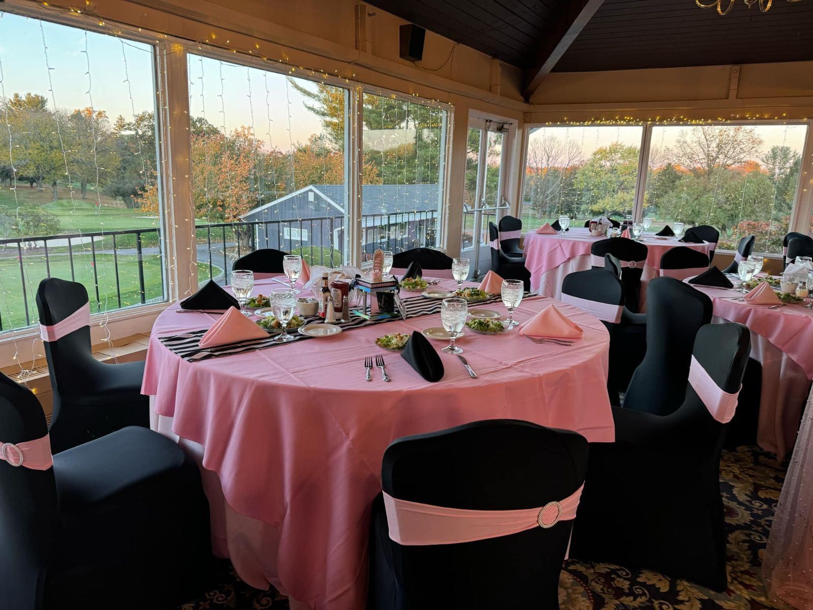 A room with pink tables and black chairs set up for a wedding reception.