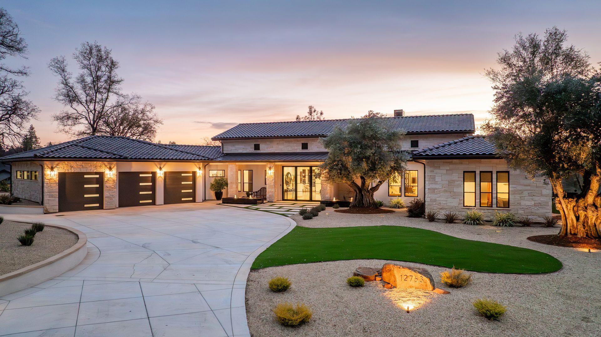 One of the luxury homes in Auburn, CA, with a sleek design, circular driveway, and glowing sunset lights.