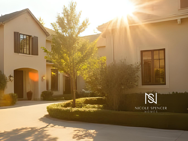 Sunlit exterior of a beige stucco home with brown shutters, manicured hedges, and a circular driveway.