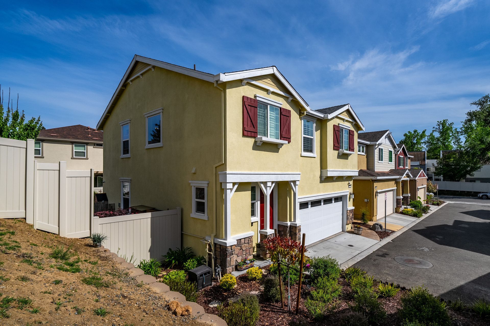Two-story home with yellow exterior, attached garage, and fresh landscaping featured by Nicole Spencer—GUIDE Real Estate.