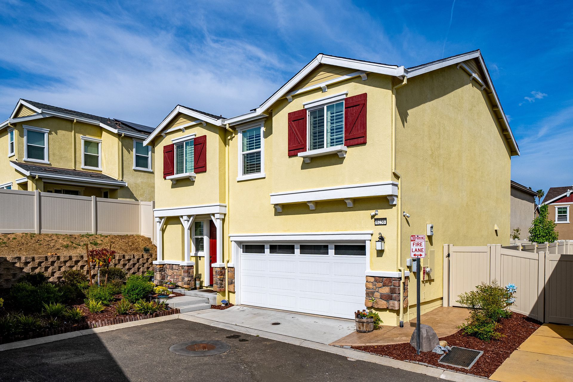 Front view of two yellow two-story homes with white trim, attached garages, and manicured landscaping on a sunny day.