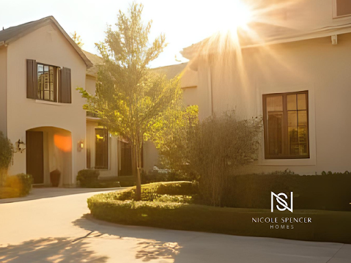 Sunlit exterior of a beige stucco home with brown shutters, manicured hedges, and a circular driveway.